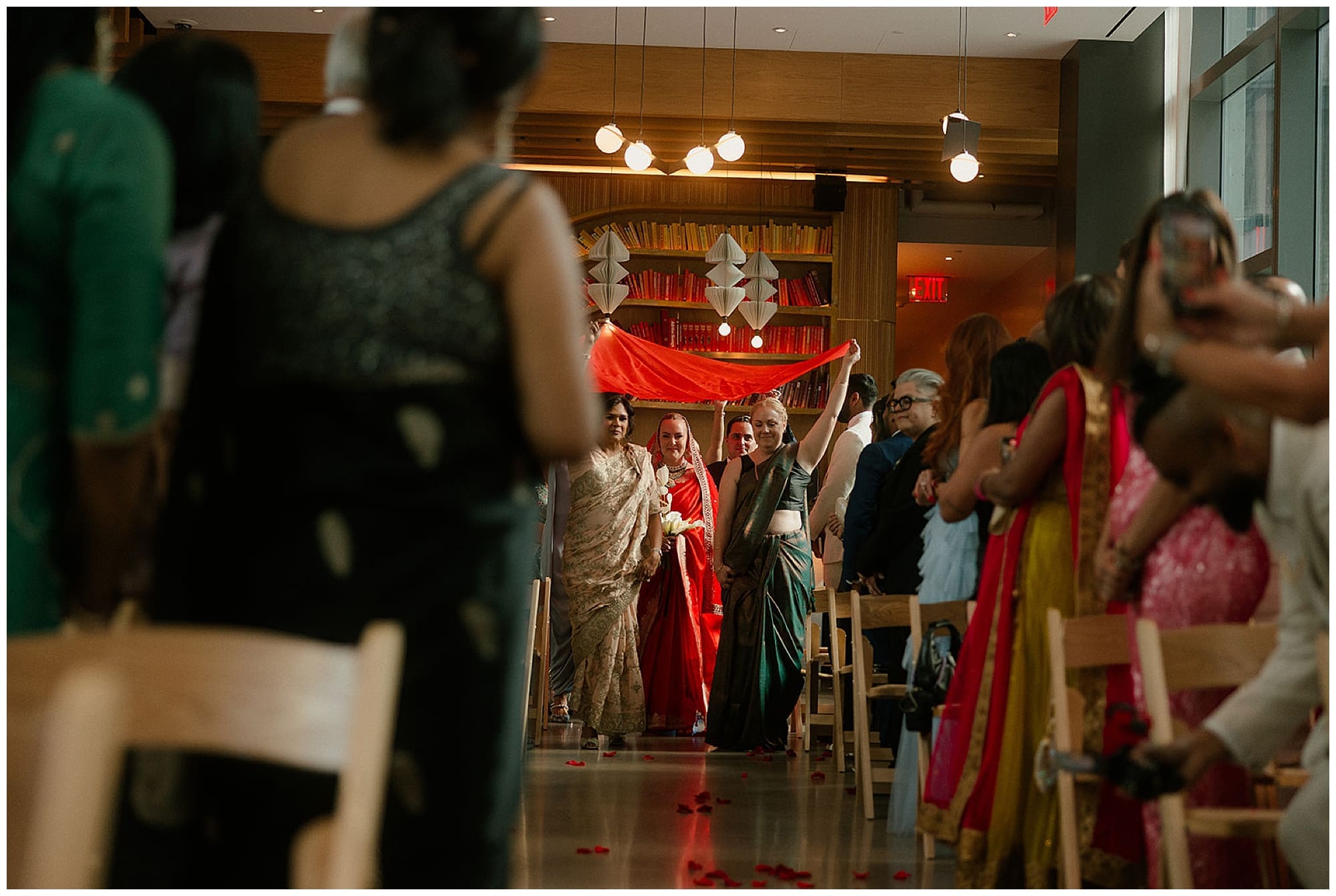 Guests and family gather during the Hindu wedding ceremony at Virgin Hotels NYC, with the lush red floral mandap visible in the background. The warmth and energy of the New York City celebration fills the room.