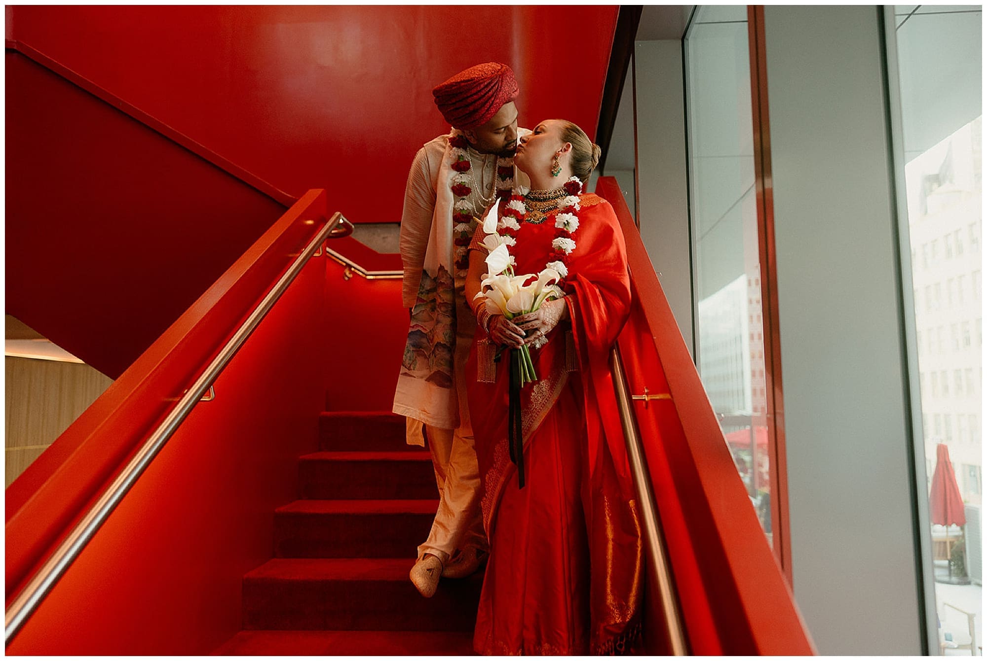 The couple shares an intimate portrait on the dramatic angular red staircase at Virgin Hotels NYC. The bold crimson architecture of this Manhattan hotel creates a striking backdrop for this New York City wedding day moment.