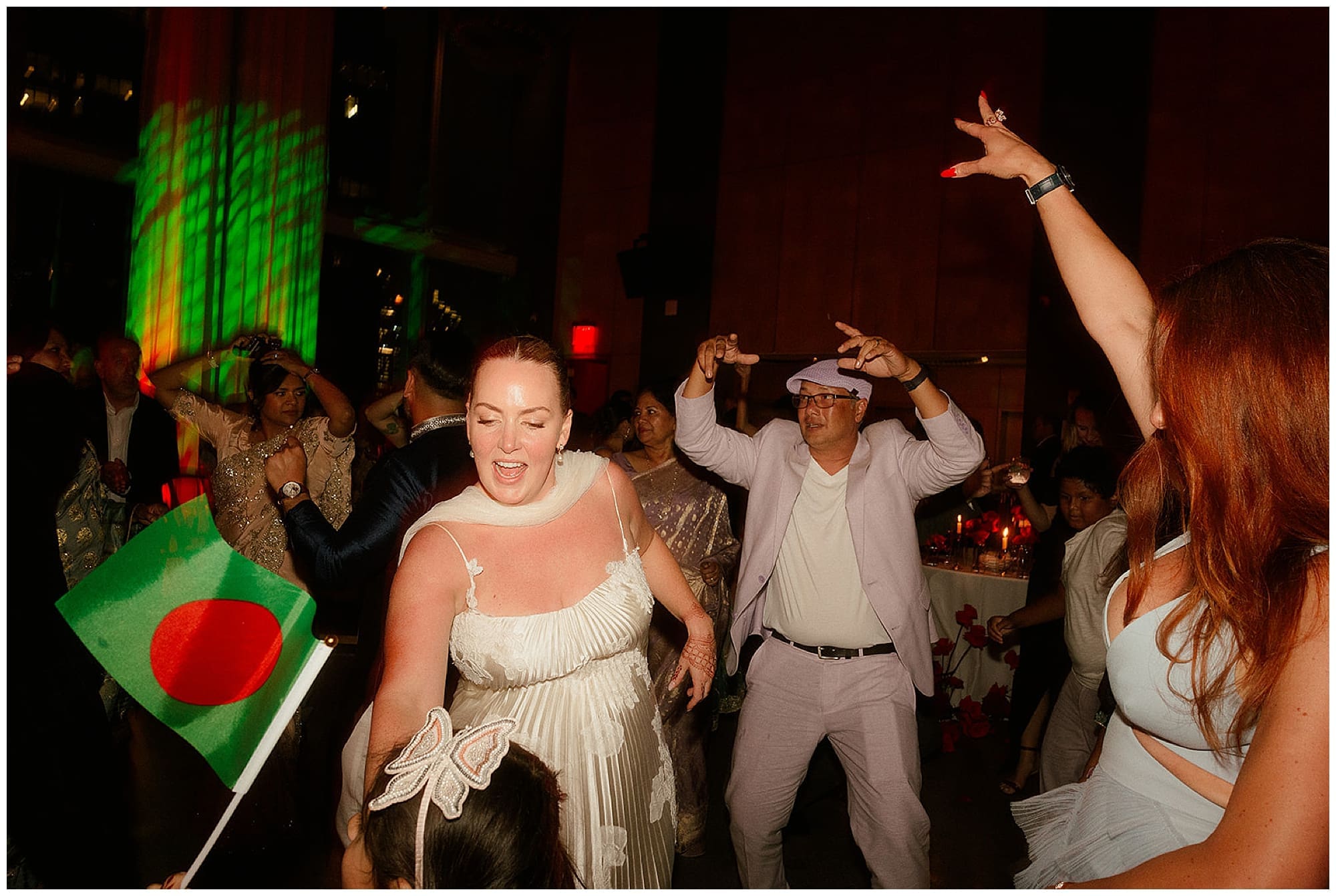The bride dances with guests on a packed dance floor at Virgin Hotels NYC in Manhattan, bathed in dramatic red reception lighting. The energy of this New York City wedding celebration is electric.