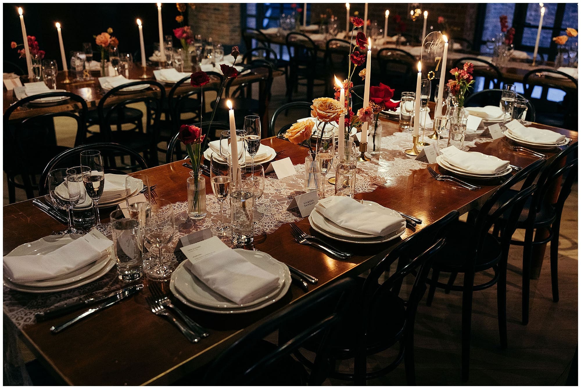 The reception tables at the Wythe Hotel in Brooklyn, New York, are dressed with dramatic floral centerpieces in deep red and burgundy tones, surrounded by warm candlelight for this moody and romantic NYC wedding.