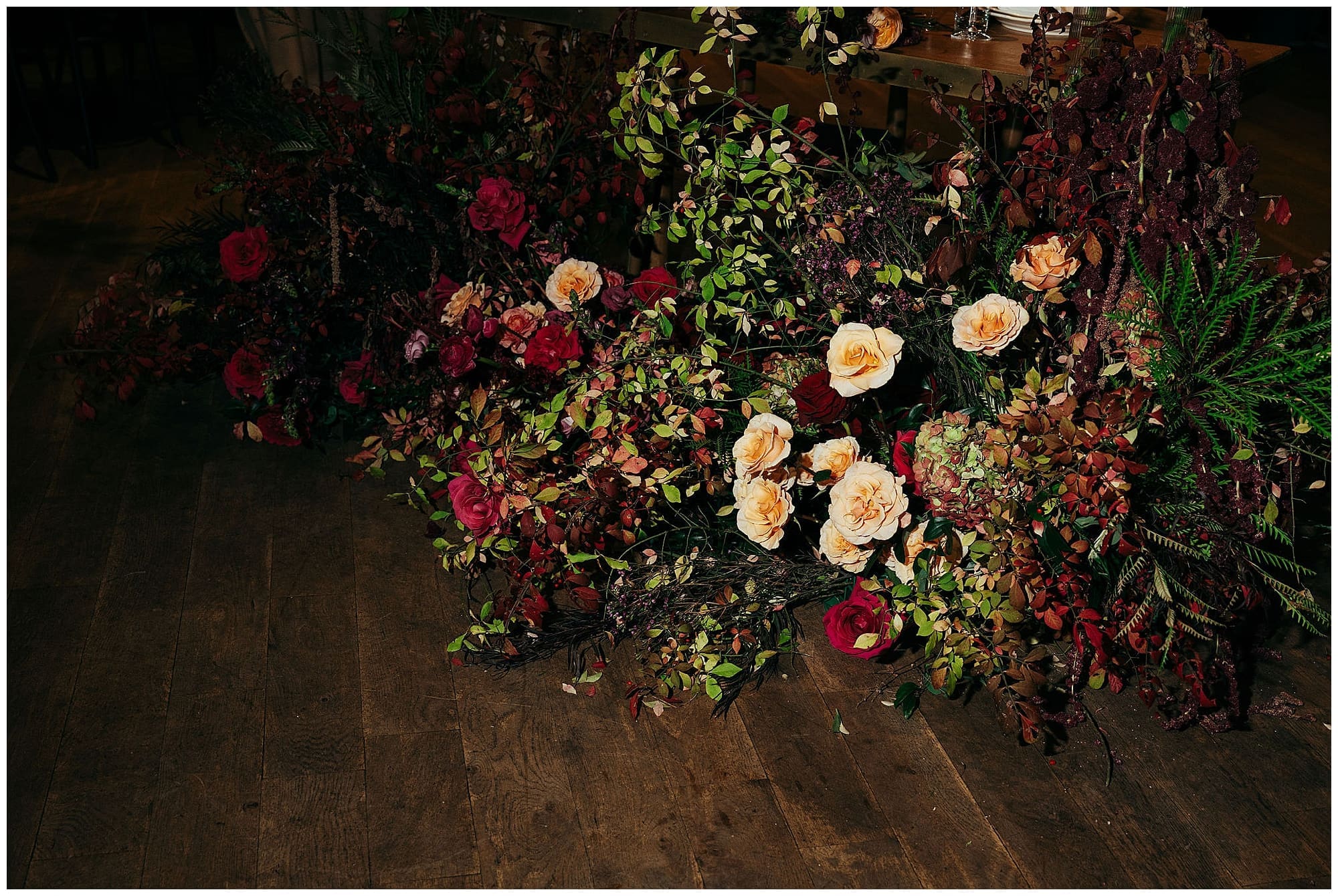 A lush close-up of the wedding floral arrangement featuring deep red, burgundy, orange, and blush blooms cascading against a backdrop of greenery, crafted by the couple's New York City wedding florist for this Wythe Hotel Brooklyn wedding.